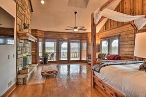 A log cabin-style bedroom with a wooden bed, a ceiling fan, and a stone fireplace. - Hot Tub, Grill: Hilltop Log Cabin in Hot Springs! (Hot Springs)