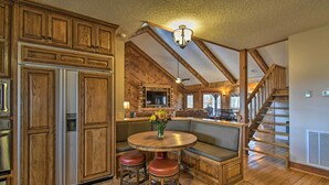 A spacious kitchen with wooden cabinetry, a central island with stools, a built-in seating area, and a staircase leading to an upper level. - Hot Tub, Grill: Hilltop Log Cabin in Hot Springs! (Hot Springs)