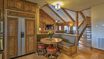 A spacious kitchen with wooden cabinetry, a central island with stools, a built-in seating area, and a staircase leading to an upper level.