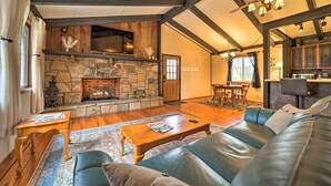 A cozy living room with a stone fireplace, wooden beams, a leather sofa, and a dining area. - 'stonewood Lodge' Couples Retreat in Glenville! (Glenville)