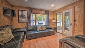 A room with a wooden paneled wall, a leather sofa, a television, and a large window with curtains. - 'james West' Apt w/ 50 Acres Near Raystown Lake (Huntingdon)
