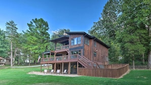 A two-story wooden house with a balcony and a deck, surrounded by a grassy yard and trees. - Waterfront Beaver Lake Hideaway w/ Kayaks & More! (Springdale)