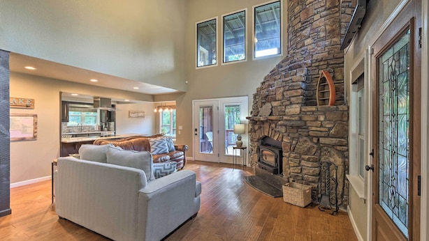 A spacious living room with a stone fireplace, a sofa, and a kitchen in the background. - Waterfront Beaver Lake Hideaway w/ Kayaks & More! (Springdale)