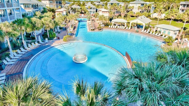 Ein großer Swimmingpool mit einem kreisförmigen Wasserspiel, umgeben von Palmen und Liegestühlen.