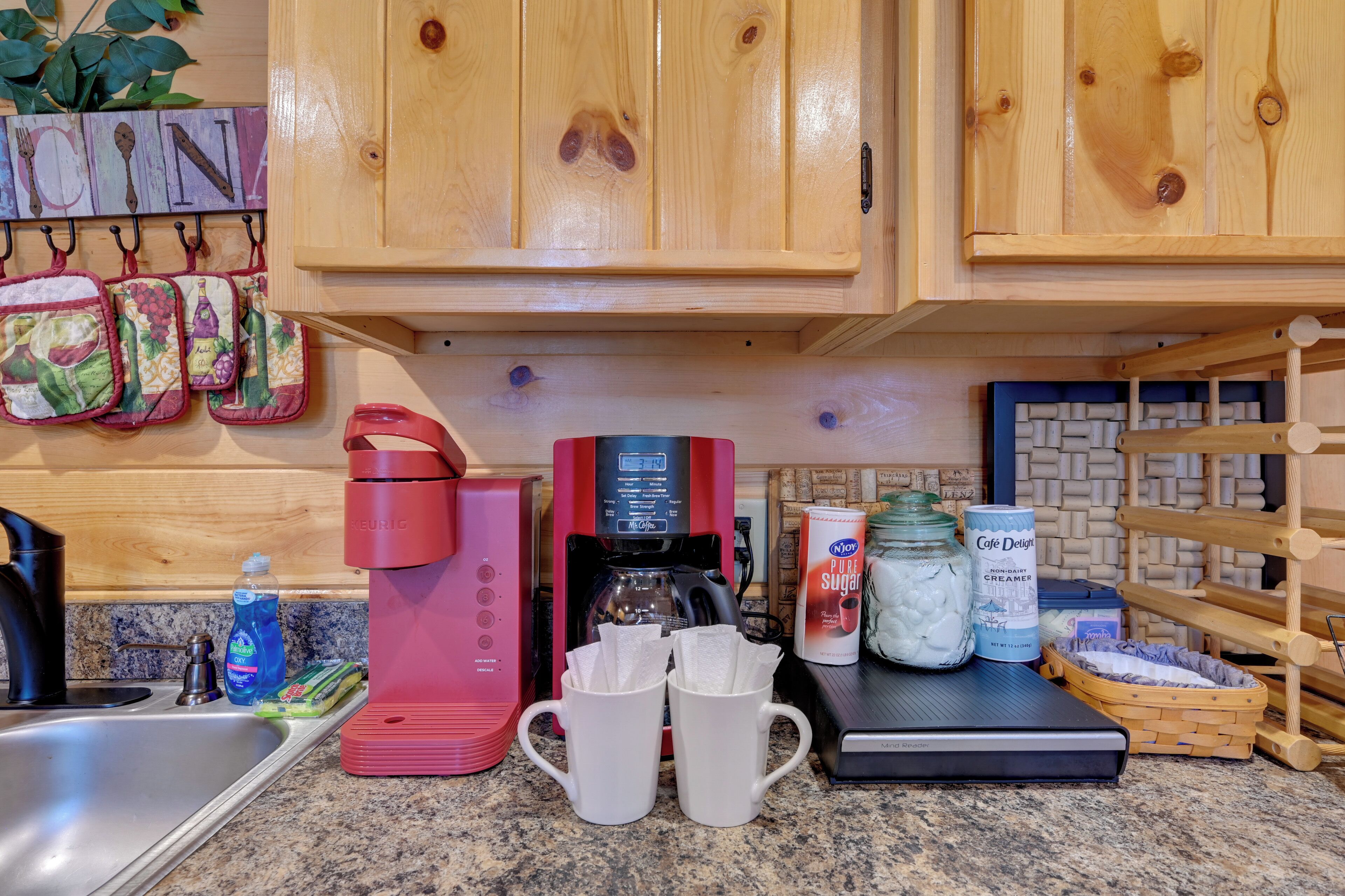 A kitchen with wooden cabinets, a coffee maker, mugs, and various kitchen items.