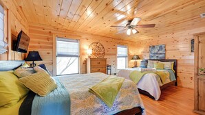 Ein Schlafzimmer in einer Holzhütte mit zwei Betten, einem Deckenventilator und einem Kamin.