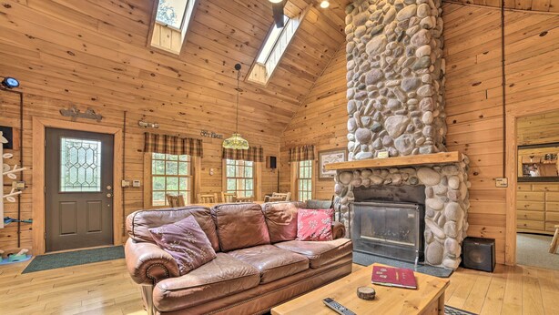 A cozy log cabin interior with a stone fireplace, leather sofa, and wooden furniture. - Riverfront Lewiston Cabin w/ Stone Fireplace! (Mio)