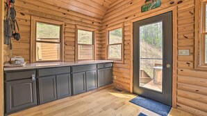 A cabin interior with wooden walls, a kitchen counter, cabinets, and a door leading outside. - Riverfront Lewiston Cabin w/ Stone Fireplace! (Mio)