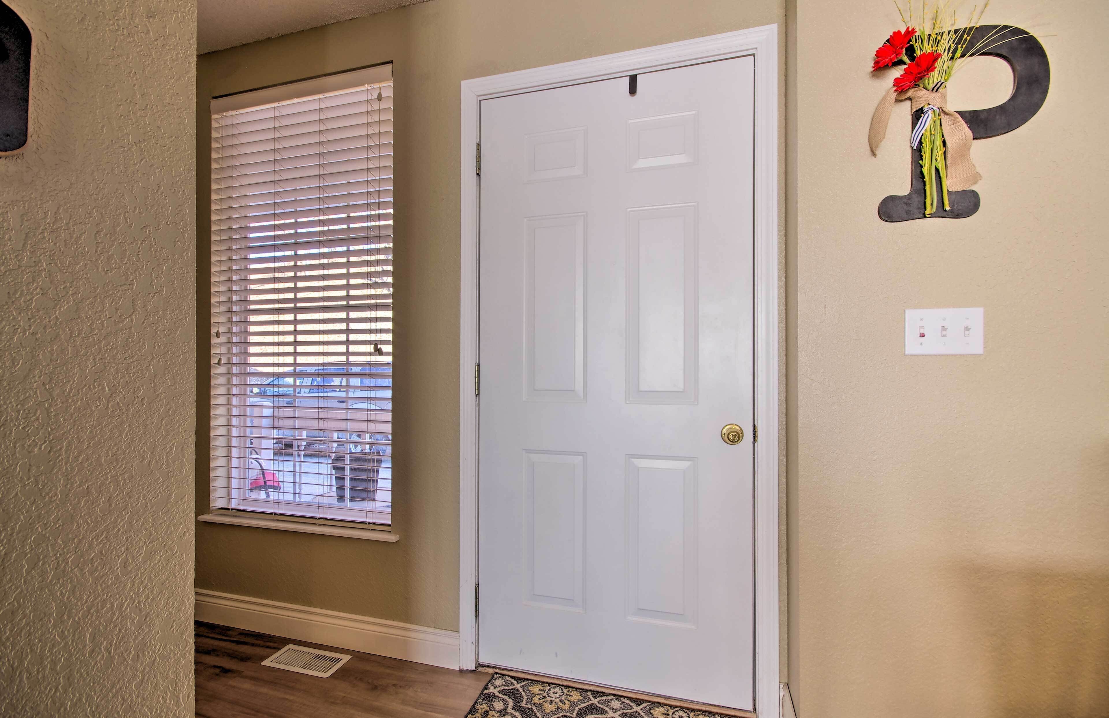 A hallway with a white door, a window with blinds, and a wall decoration of a letter 'P' with flowers.