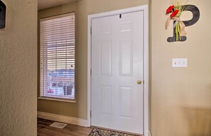 A hallway with a white door, a window with blinds, and a wall decoration of a letter 'P' with flowers.