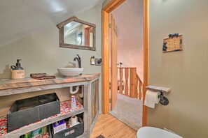 Un baño con tocador de madera, un lavamanos, un espejo, un perchero para toallas y un inodoro.