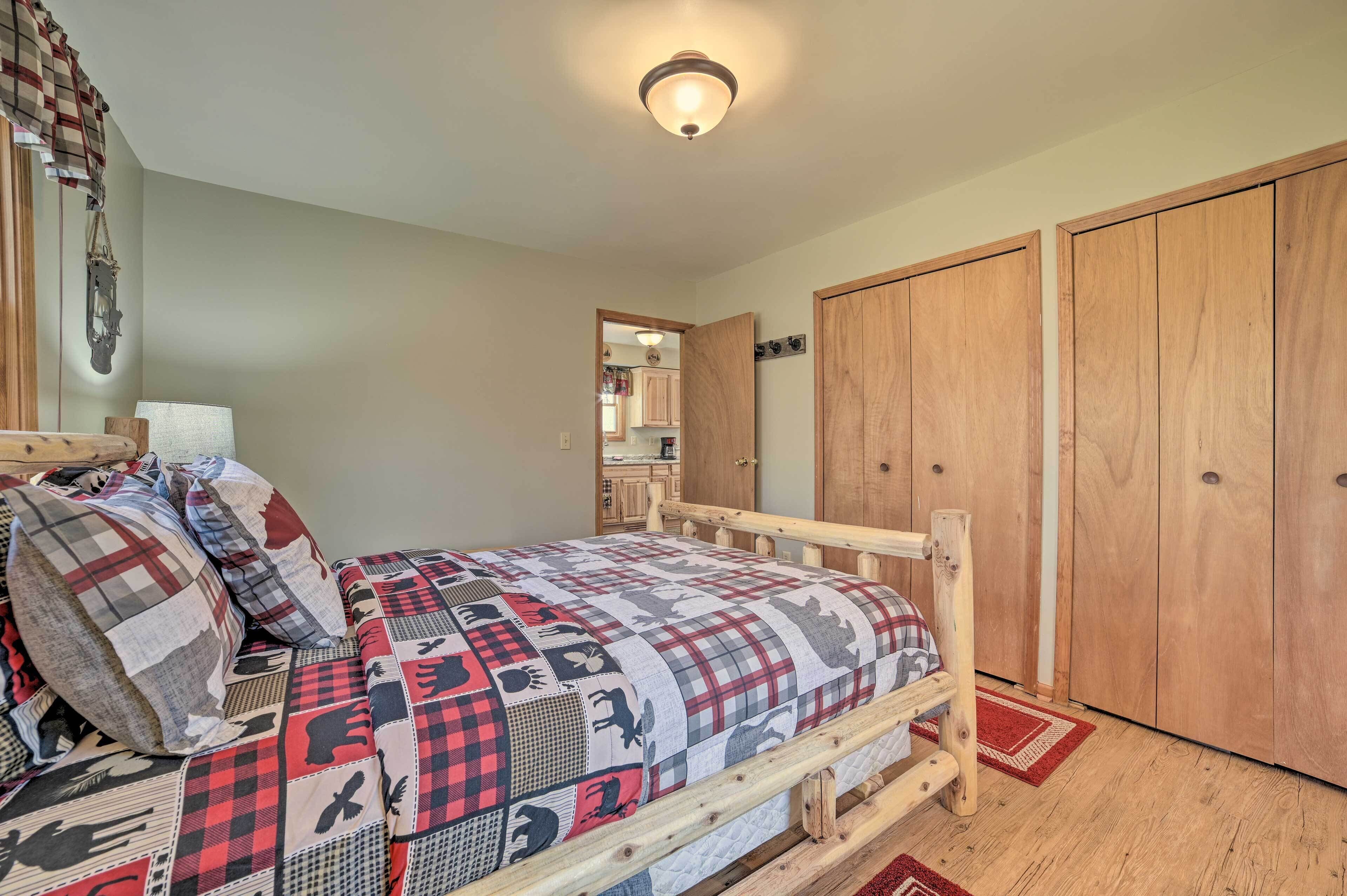 A bedroom with a wooden bed, a red and black checkered bedspread, a wooden wardrobe, and a red rug.