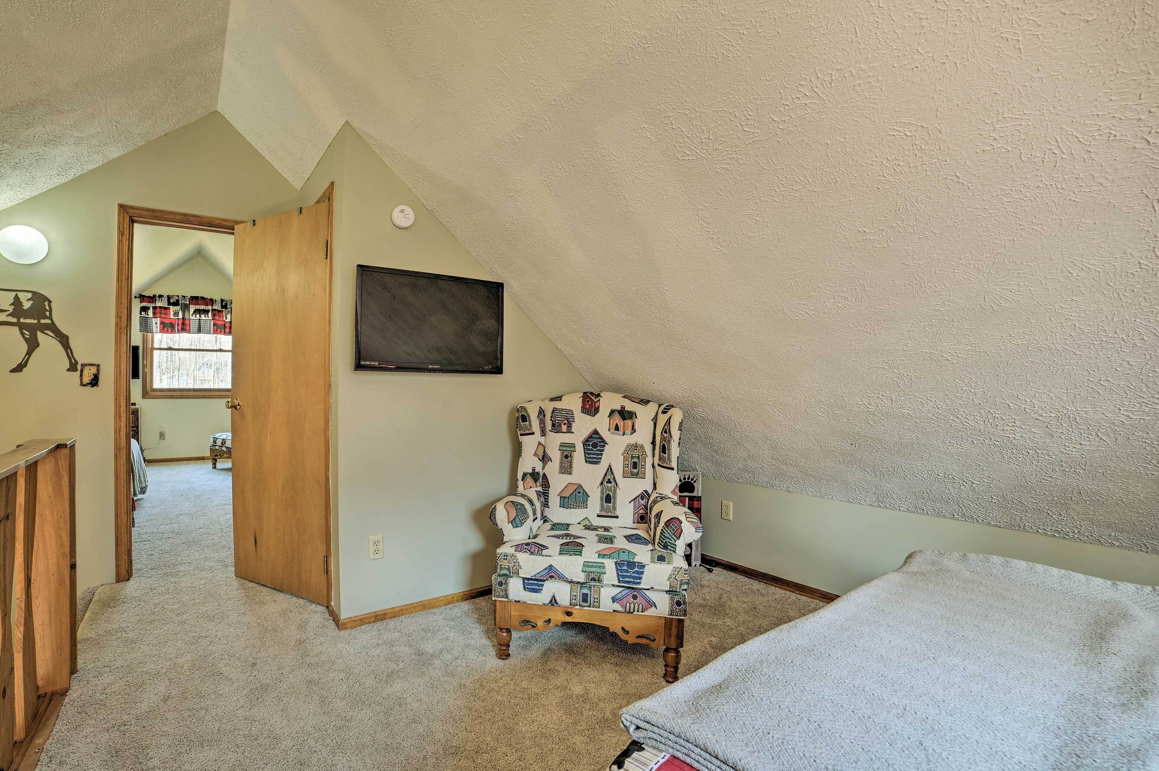 Een kamer met een hoge plafond, een gestreept fauteuil, een flatscreen televisie en een deur naar een andere kamer.