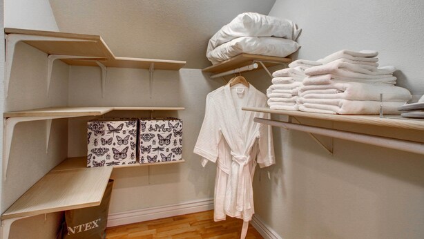 A storage closet with shelves, a hanging robe rack, and neatly stacked towels. - Monument Retreat - Walk to Local Dining & Shopping (Monument)