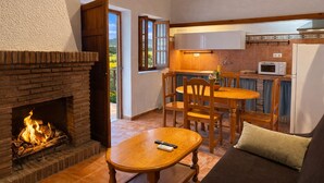 A cozy living room with a fireplace, a dining area with wooden furniture, and a kitchen with a microwave. - Cozy Apartment El Pajar near El Chorro (El chorro)