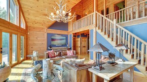 Amplio interior de cabaña de madera con una gran sala de estar, una escalera y un televisor.