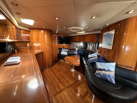 A luxurious interior with a wooden floor, a black leather sofa with decorative pillows, a wooden bar area, and a mounted television.