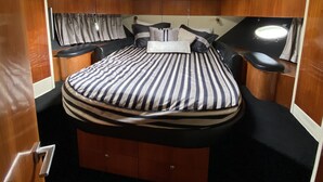 Un dormitorio pequeño y luminoso con una claraboya circular, una cama a rayas y muebles de madera.