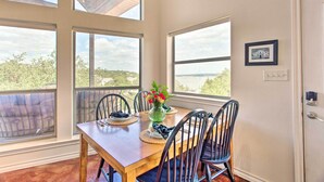 Un comedor con una mesa de madera, cuatro sillas, un florero con flores y ventanas amplias con vistas al exterior.