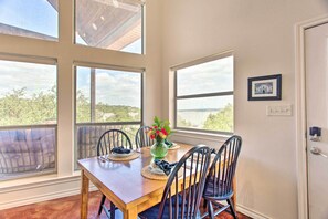 A dining area with a wooden table, four chairs, a vase with flowers, and large windows offering a view of the outdoors. - Waterfront Home w/ Boat Dock on Lake Granbury! (Granbury)