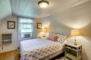 Um quarto com uma cama, duas luminárias de cabeceira, uma janela com cortinas de renda e um ar condicionado fixado na parede.