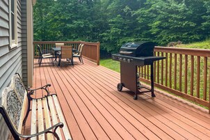 Una terraza de madera con una parrilla, sillas y un banco.
