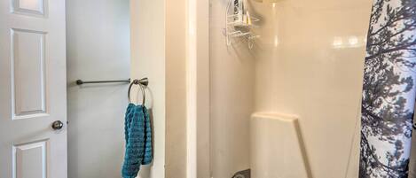 Een badkamer met een douche, een handdoekrek met een blauwe handdoek en een deur met een deurklink.