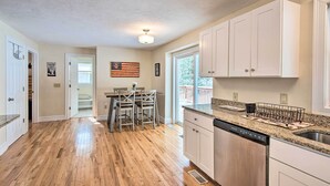 Una cocina amplia con suelo de madera, armarios blancos y encimera de granito.
