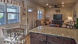 A kitchen with a granite countertop, a dining table with chairs, a ceiling fan, and a television. - Charming Cabin w/ Patio - Walk to Table Rock Lake! (Lampe)