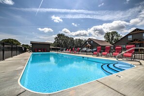 A swimming pool with red lounge chairs and a building in the background. - Charming Cabin w/ Patio - Walk to Table Rock Lake! (Lampe)