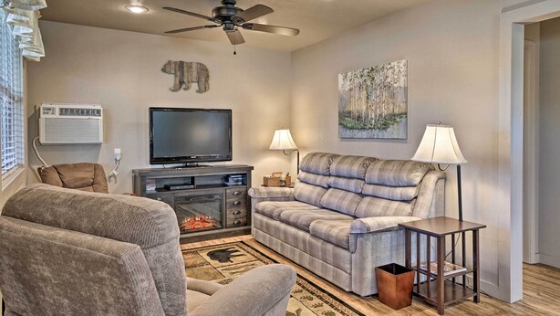 A living room with a fireplace, a sofa, a television, and a ceiling fan. - Charming Cabin w/ Patio - Walk to Table Rock Lake! (Lampe)