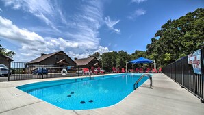 A swimming pool with a blue water feature, surrounded by a concrete deck and a metal fence. - Charming Cabin w/ Patio - Walk to Table Rock Lake! (Lampe)