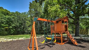 A wooden swing set with a slide and a climbing structure in a park. - Charming Cabin w/ Patio - Walk to Table Rock Lake! (Lampe)