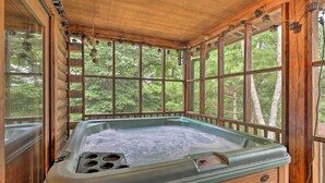 Un jacuzzi en una cabaña de troncos con ventanas amplias y vigas de madera.