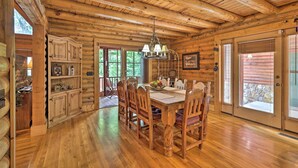 Interior de una cabaña de madera con una mesa de comedor, sillas y una araña.