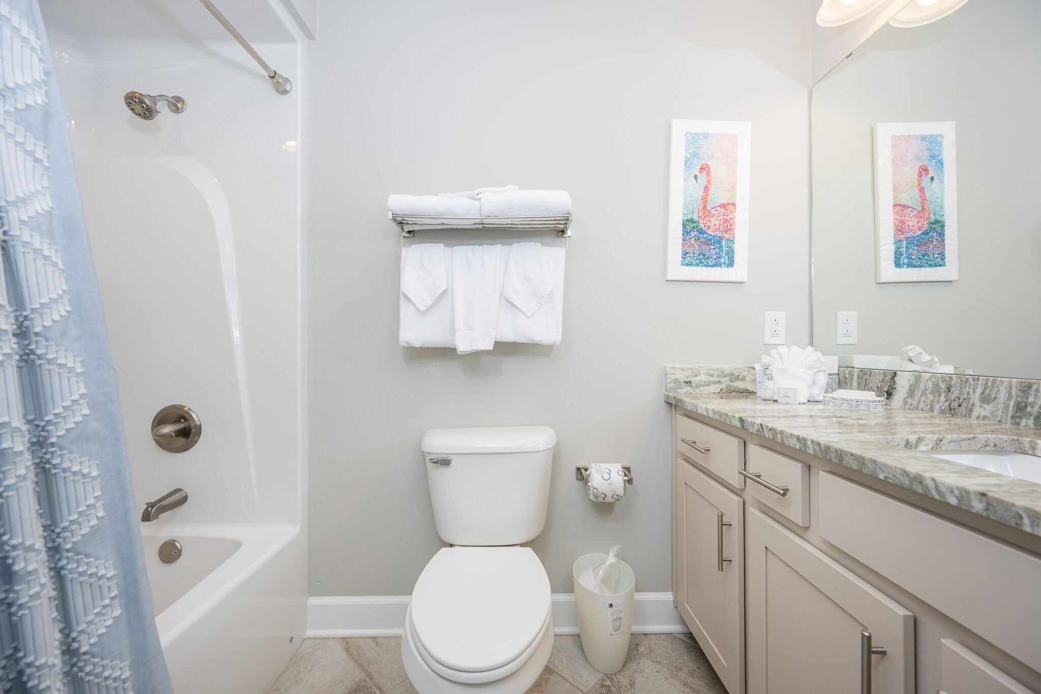 A bathroom with a bathtub, toilet, and sink. There are towels hanging on a rack, and a trash can is visible.