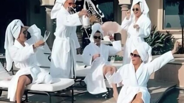 A poolside gathering with people in white robes, a clear pool, and a building with a tiled roof in the background.
