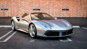 A silver sports car parked in a parking space with a brick wall background and reserved suite signs.