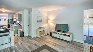 Een moderne keuken met witte kasten, een eethoek met een tafel en stoelen, en een woonkamer met een televisie en een lamp.