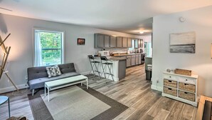 Een moderne woonkamer met een grijze bank, een witte salontafel, en een keuken met grijze kasten en een wit eiland.