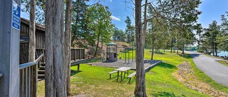 A wooden deck with picnic tables and a gazebo, surrounded by trees and a lake view.
