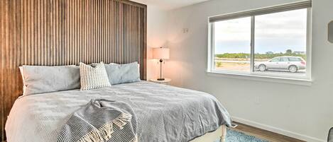 A bedroom with a bed, a lamp, a window, and a view of the outside.