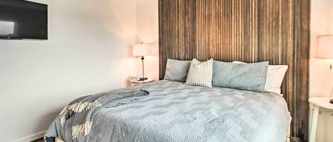 Une chambre moderne avec un grand lit, une tête de lit en bois, deux tables de chevet avec des lampes et un téléviseur à écran plat fixé au mur.