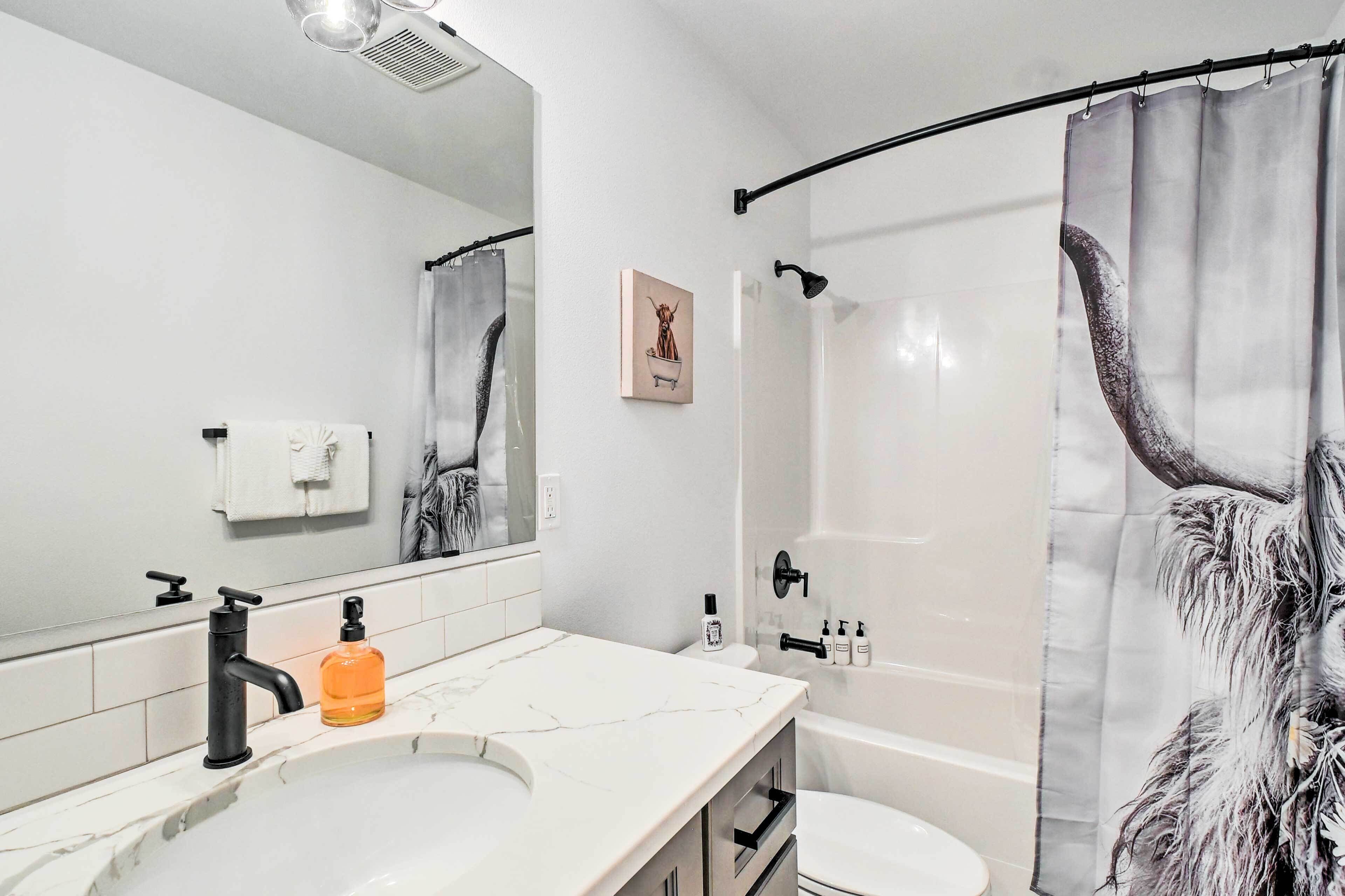 Un baño moderno con un lavabo blanco, grifo negro y cortina de ducha con un diseño de animal mullido.
