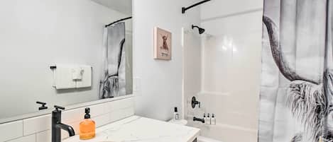 Un baño moderno con un lavabo blanco, grifo negro y cortina de ducha con un diseño de animal mullido.