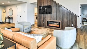 A modern living room with a fireplace, comfortable seating, and a surfboard on the wall.