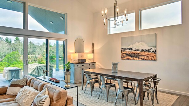 A modern living room with a large dining table, a sofa, and a view of the outdoors.