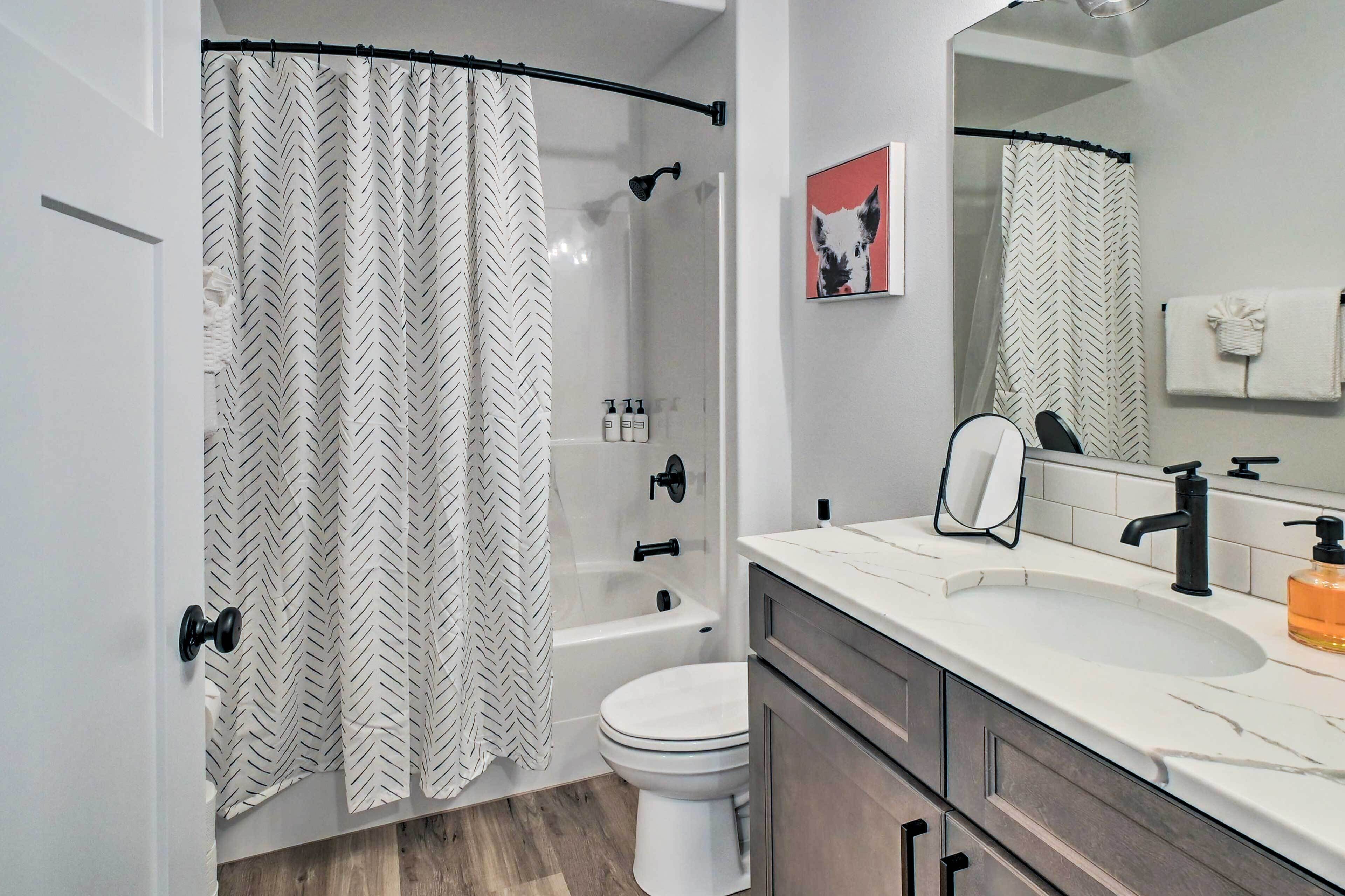 A modern bathroom with a shower curtain, a bathtub, a toilet, a sink with a mirror, and a towel rack.