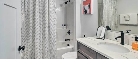 A modern bathroom with a shower curtain, a bathtub, a toilet, a sink with a mirror, and a towel rack.
