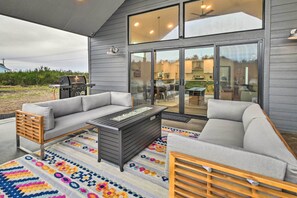 A covered outdoor seating area with a gray sofa, a wooden bench, and a coffee table.
